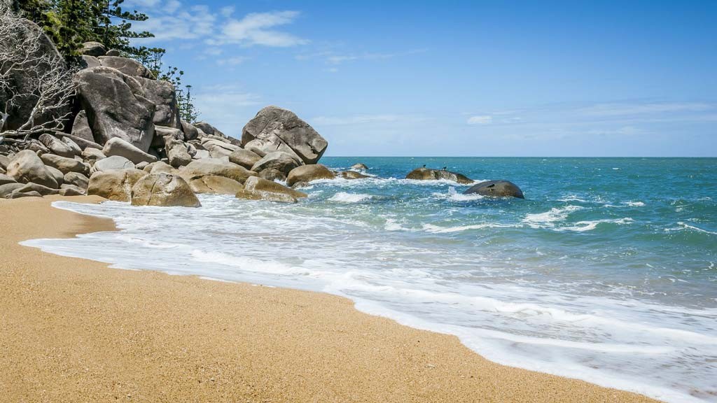 A yellow sand beach ends at a rock outcropping on Magnetic Island, Queensland.