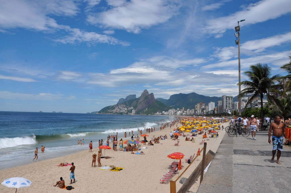 A strip of beach gets progressively more crowded with the sand full of colorful umbrellas.