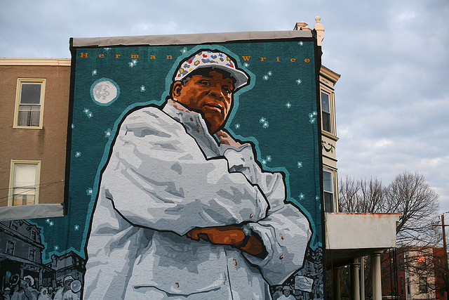 Mural of an African-American man in a white coat and ball cap painted on the side of a three-story building.
