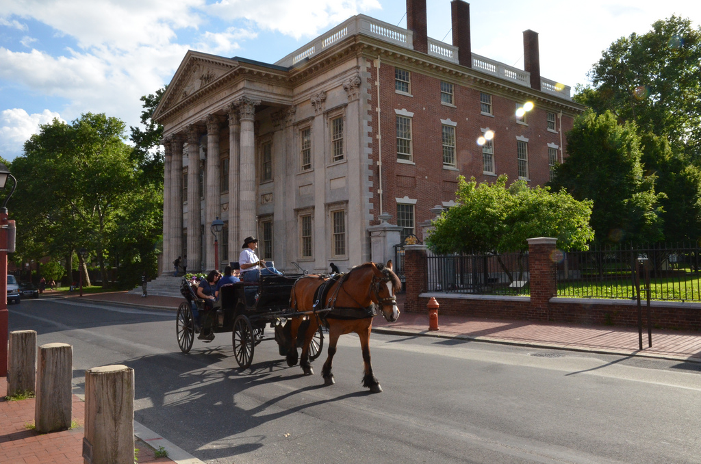 A horse-drawn carriage heads down a quiet street with a colonial building in the background.