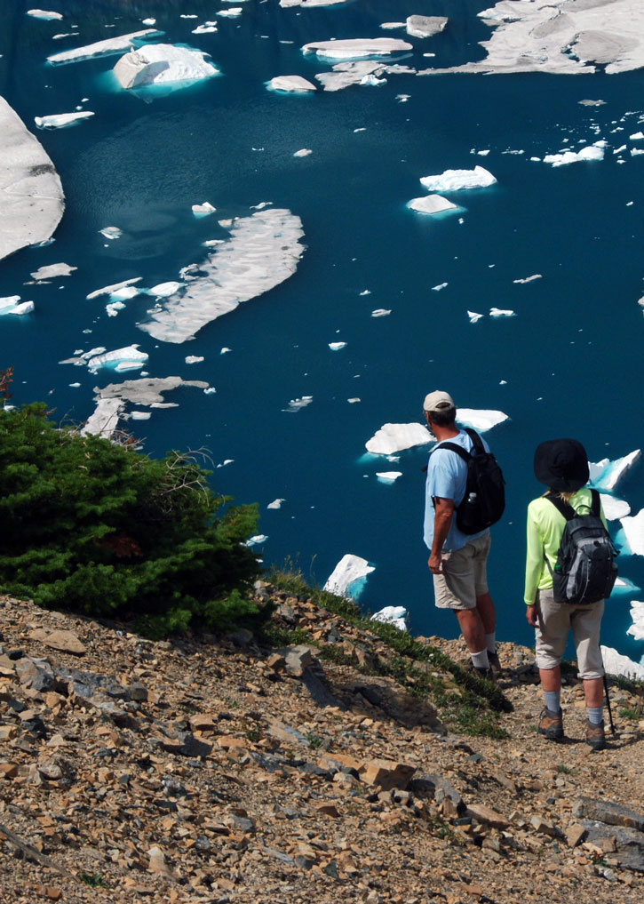 Hikers stand at the edge of Iceberg Lake in Glacier National Park.