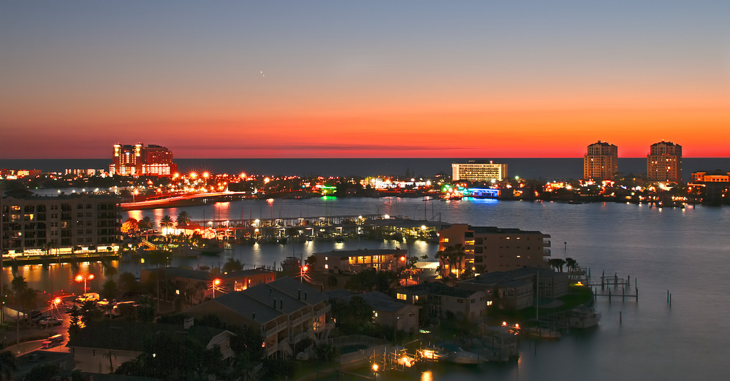 Bird's eye view of Clearwater Beach at sunset with the cityscape's lights reflecting off the water.