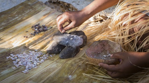 A woman makes shell money, whittling down shells into small shapes.