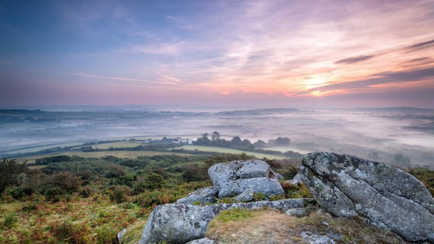 A misty sunrise over the Cornish countryside from Helman Tor, a rugged outcrop of granite moorland near Bodmin.