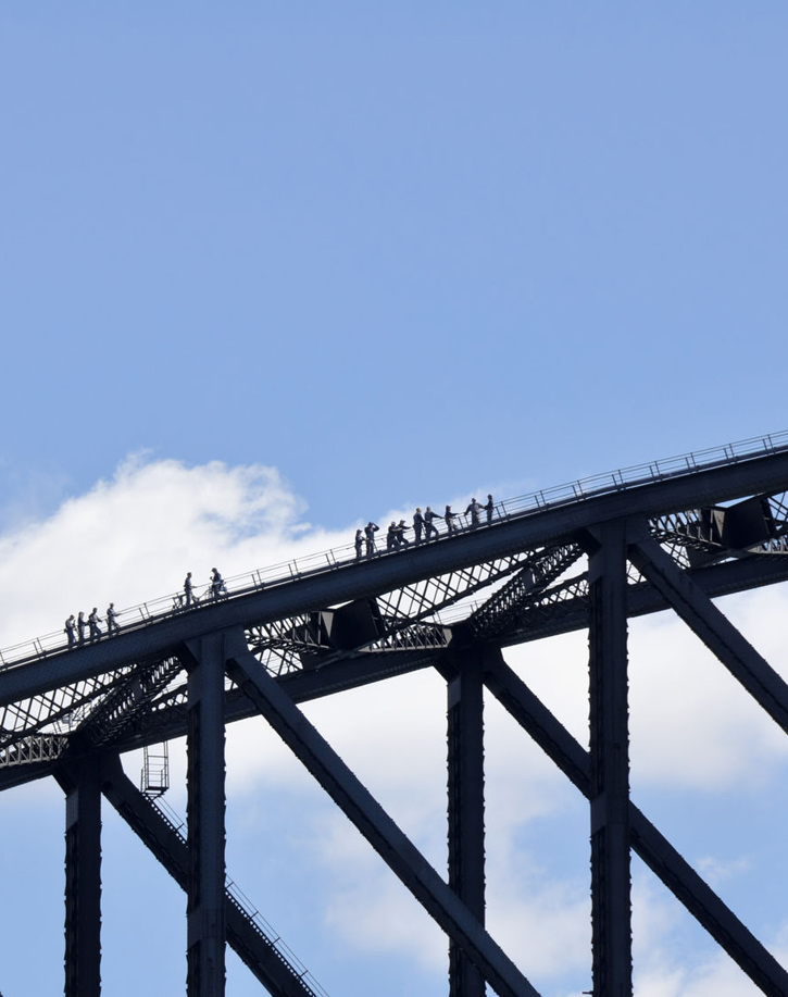 People silhouetted against a blue sky climbing Sydney's Harbour Bridge.