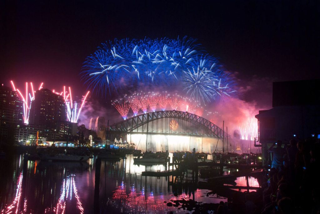 Fireworks silhouette the Sydney Harbour Bridge and boats in the harbour.