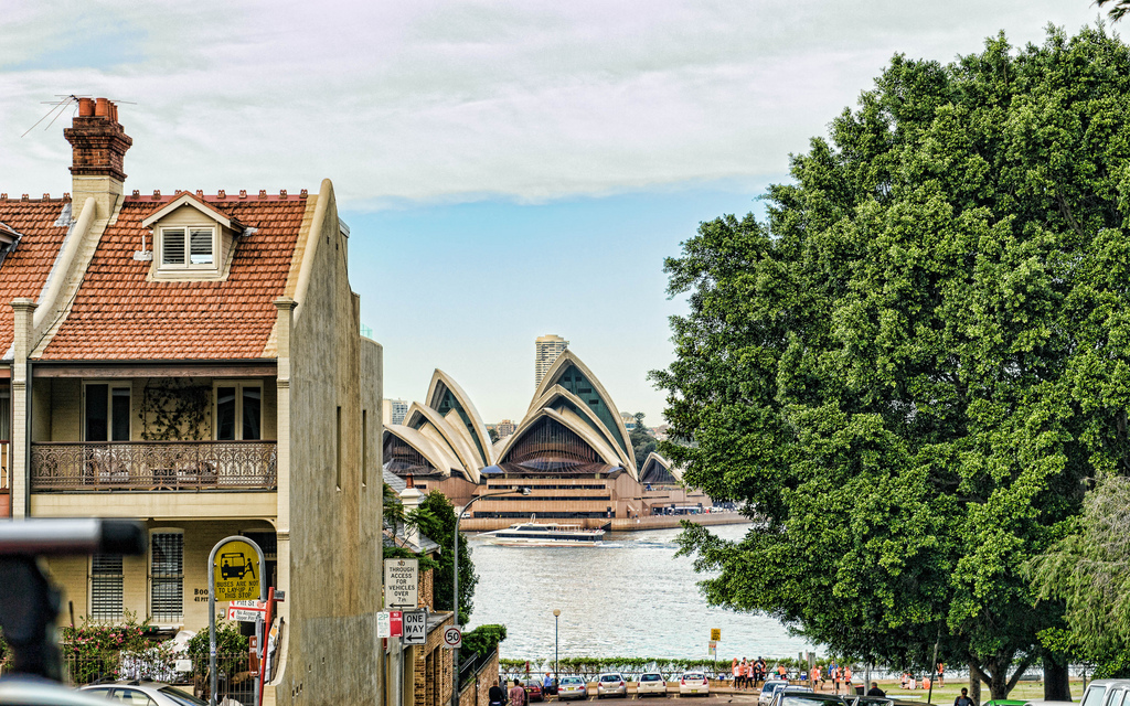 The opera house is visible across the water from a street in a neighborhood lined with townhouses.