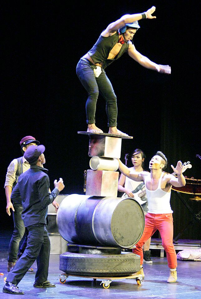 A Phare circus performer balances high on drums and boxes.