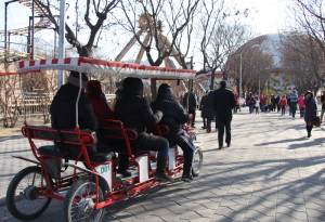 A group on a pedal-powered vehicle with bench seats rides through the park.