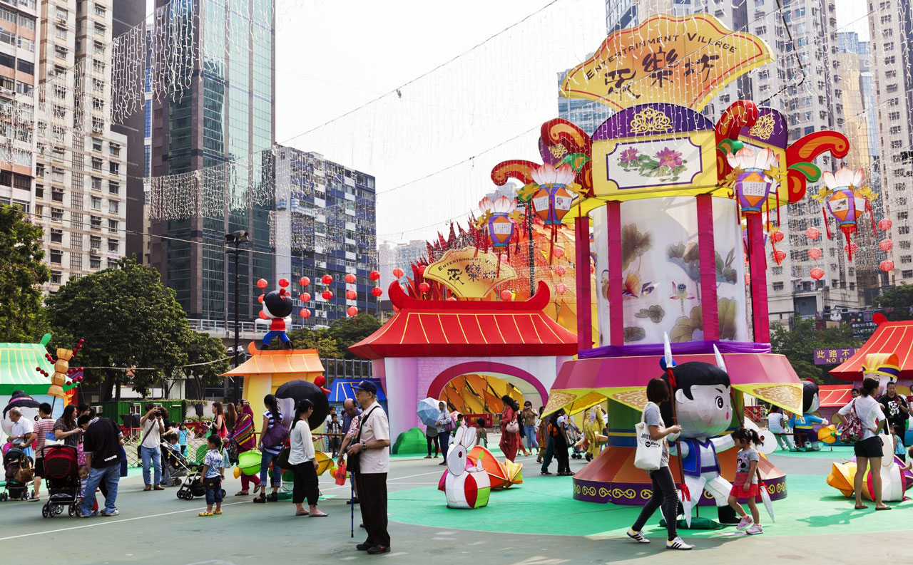 In the middle of the city, families stroll through a pop-up village with colorful characters and lanterns.