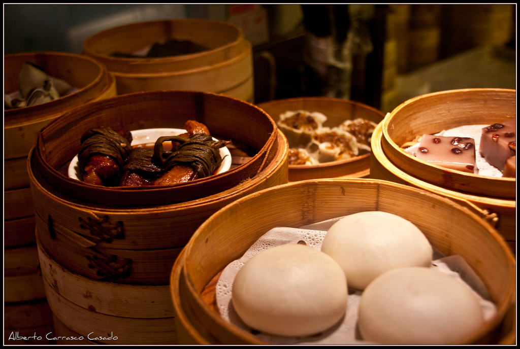 Round wooden steamer trays filled with assorted foods including dumplings and steamed buns.