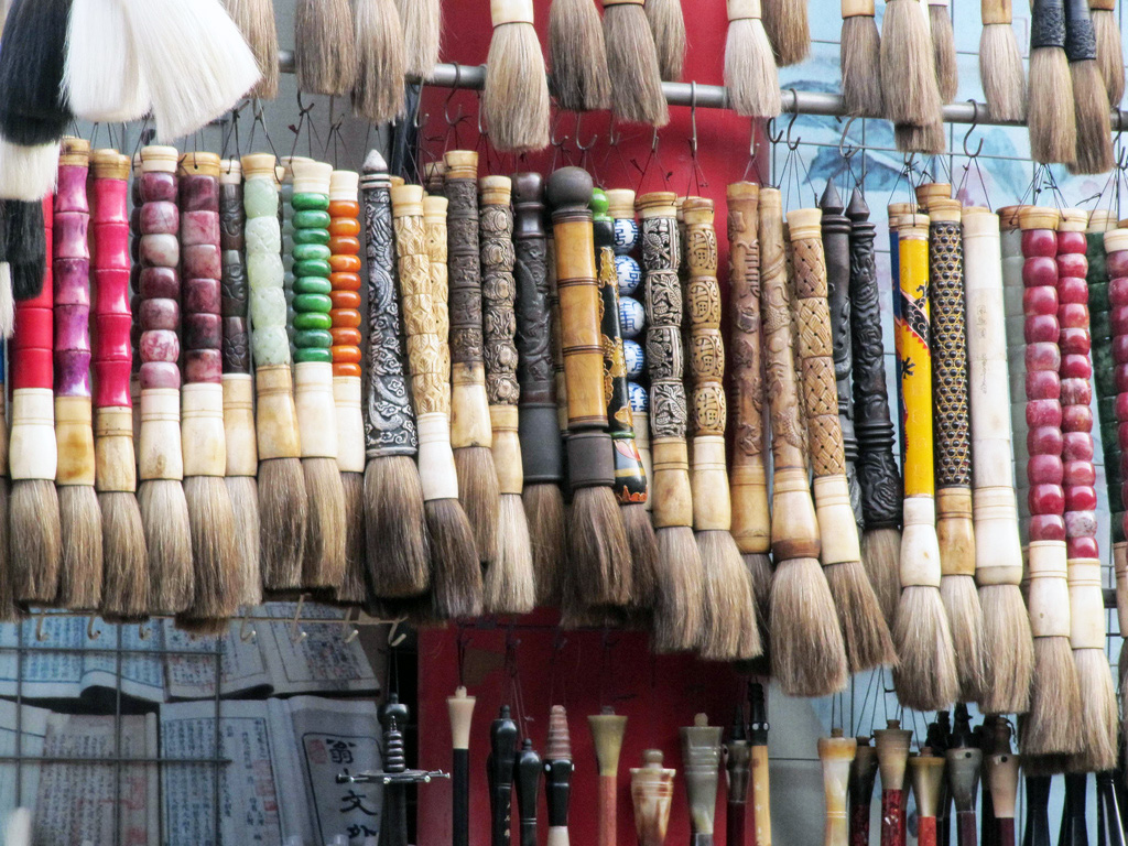 Thick writing brushes with colorful handles hang in rows in a market stall.