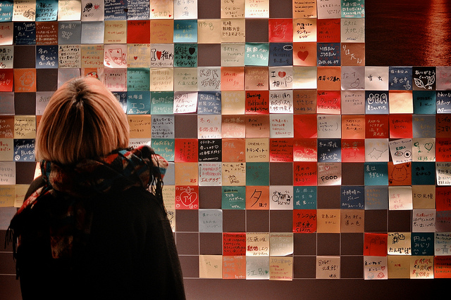 A woman stands in front of a message board made up of post-its in Hokkaido, Japan.