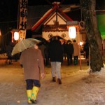 Visitors dressed for the cold and snow approach a lantern-lit shrine.