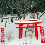 A red Torii gate stands out sharply from the snow during the day.