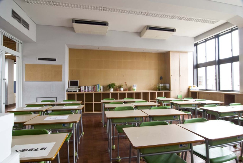 Neat rows of desks with green plastic chairs in a bright and airy classroom.