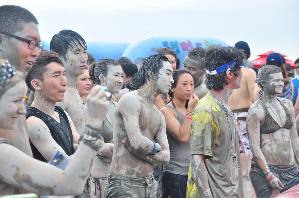 A group of young people covered from head to toe in grey mud.