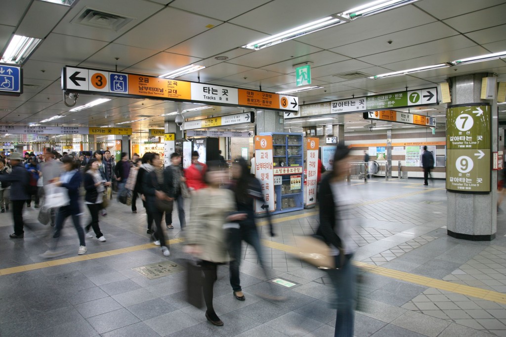 A blurred action photo of pedestrians moving through a subway terminal.