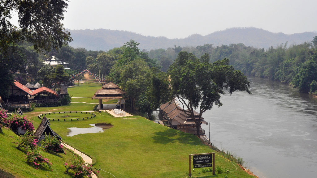 Accommodations set on the verdant banks along the slow-moving Kwai River.