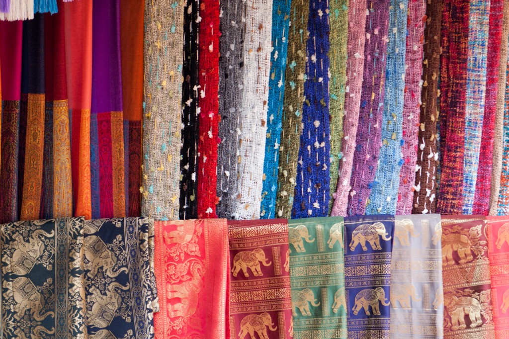 A variety of vibrant and patterned silk fabrics draped for sale.
