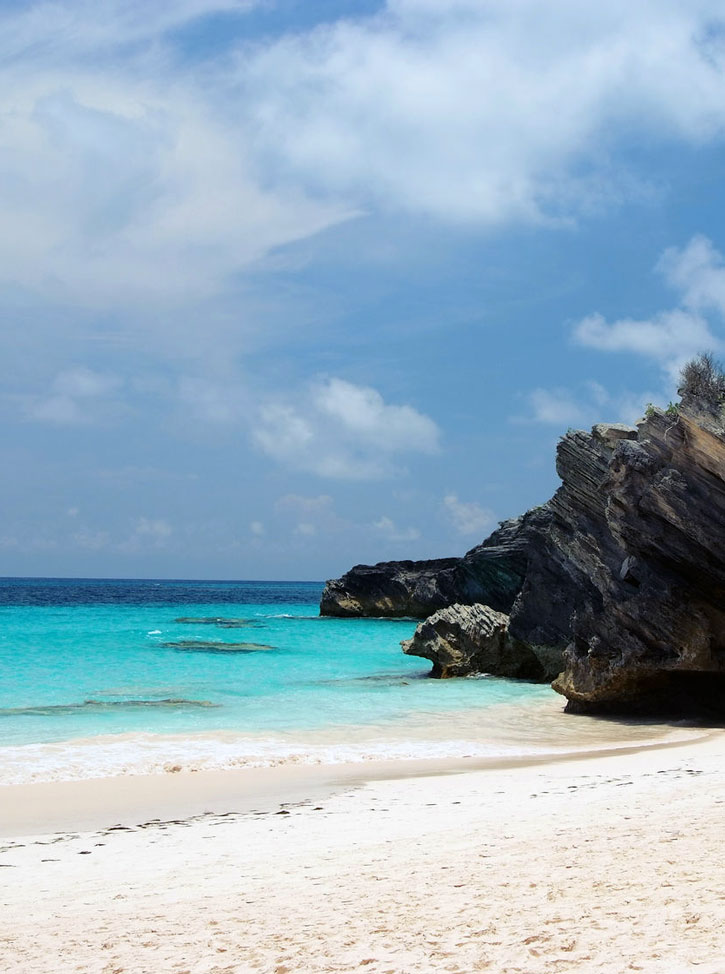 Clear water washing up on shore beside dramatic rocks in Bermuda's Horseshoe Bay.