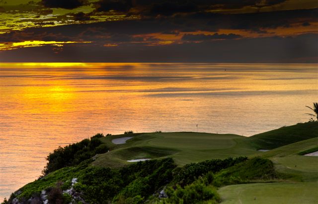 The sun sets over the water beyond a golf course perched right on the edge of the island.