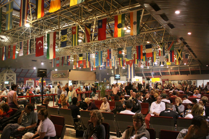 A crowded José Martí International Airport lounge is decorated with hanging flags.