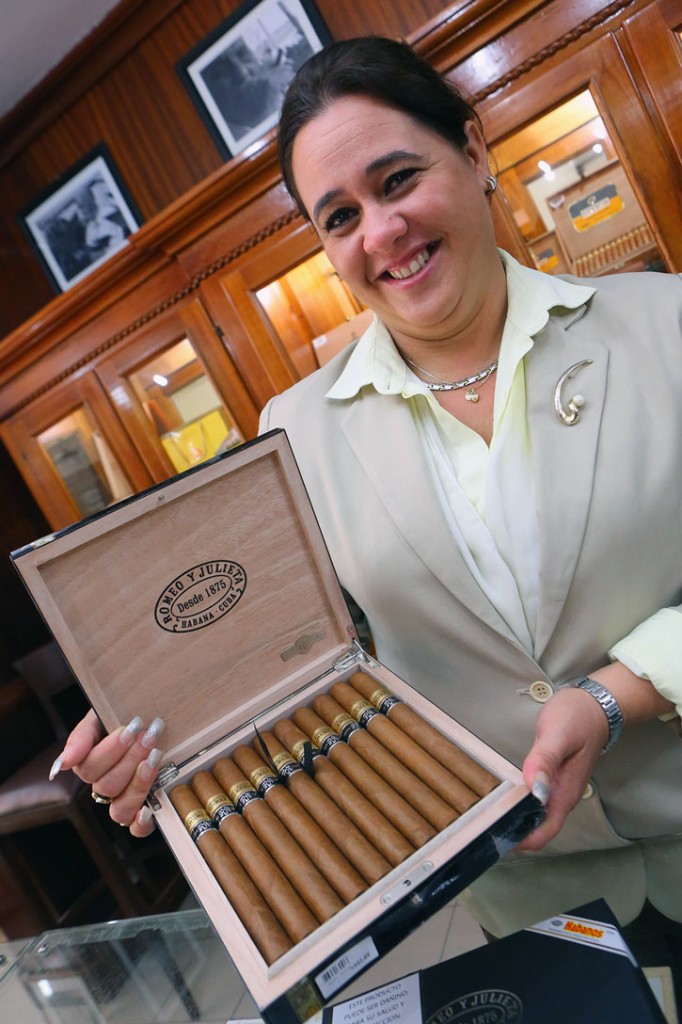 A well-dressed woman holds an open box of Cuban cigars.
