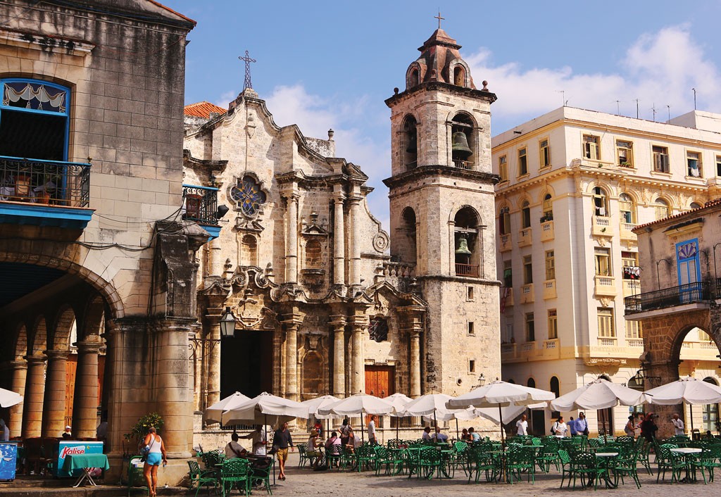 In Habana Vieja, an impressive cathedral overlooks a square filled with tables shaded by umbrellas.