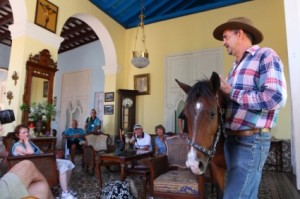 In a cowboy hat and jeans, Julio stands with a horse inside the home and addresses a group of visitors.