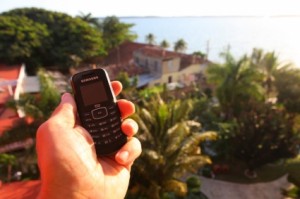 A simple bar style cellphone in a man's hand with Cuban homes in the background.