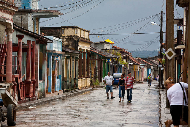 People walk down a puddle-strewn street lined with colorful colonial buildings.