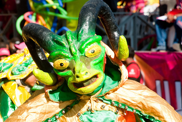 A mask of a horned green devil with bloodshot eyes and a cow-like face.
