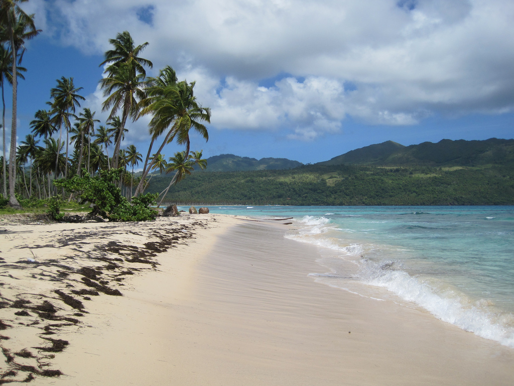 View down an unspoiled white sand beach with turquoise blue water coming up on shore.