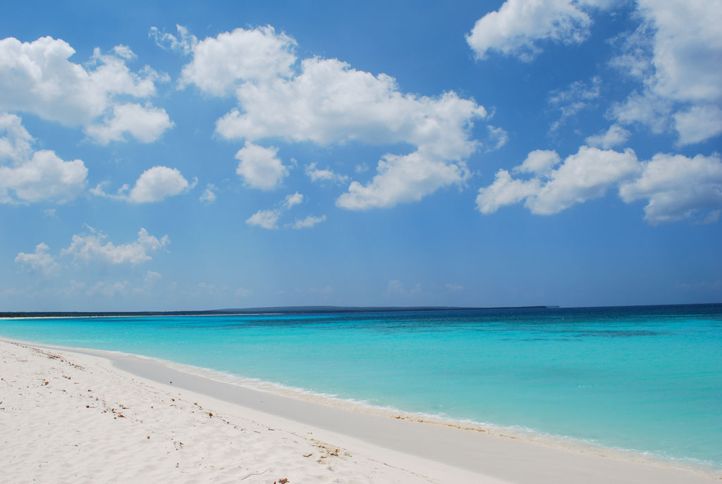 A strip of pristing white sand with calm turquoise water stretching into the distance.