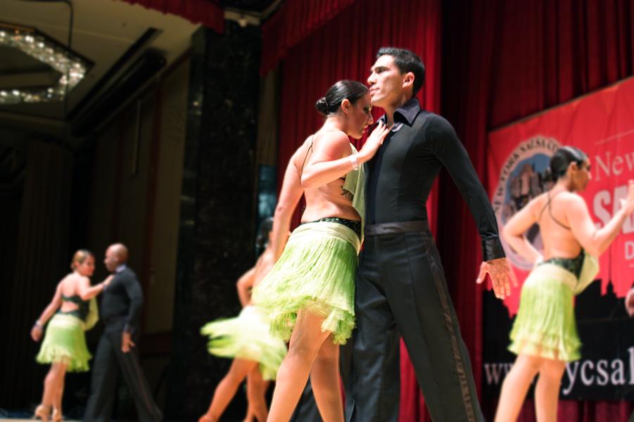 A man dressed all in black and a woman in a lime green skirt dance chest to chest.