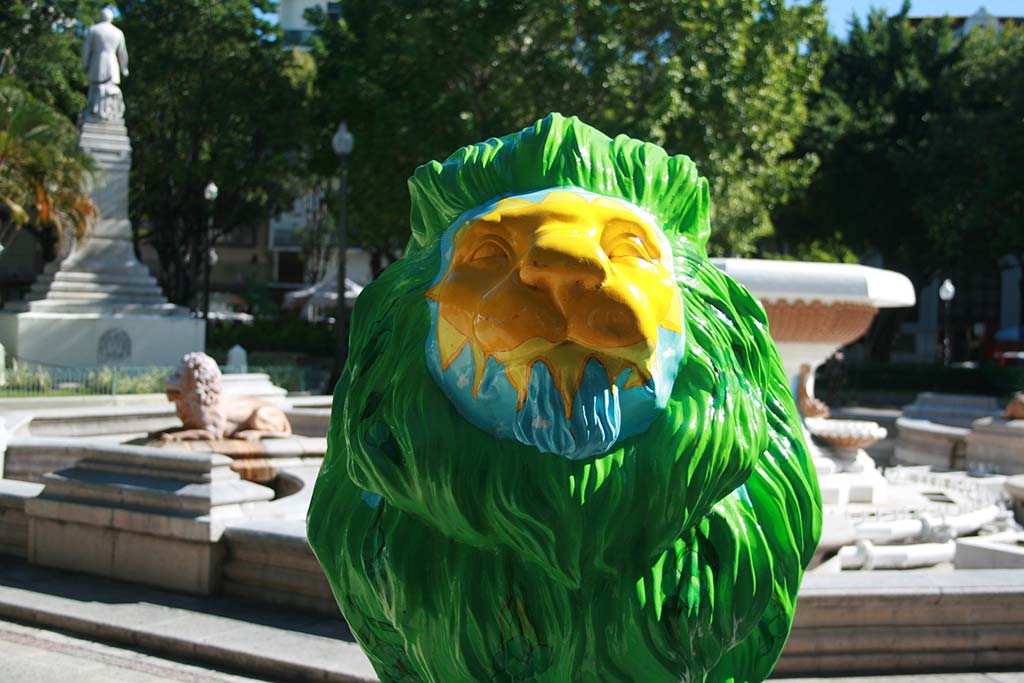 A painted lion statue and Fuentes de Leones. Photo © <a href="https://www.flickr.com/photos/micahcraig/11783032863/">Micah Craig</a>, licensed Creative Commons usage.