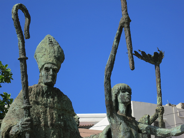 Modern bronze sculpture green and pitted of a bishop with a shepards crook and women holding torches aloft.