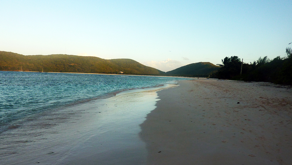 Light shines on wet sand on a pristine beach lapped by gentle waves.