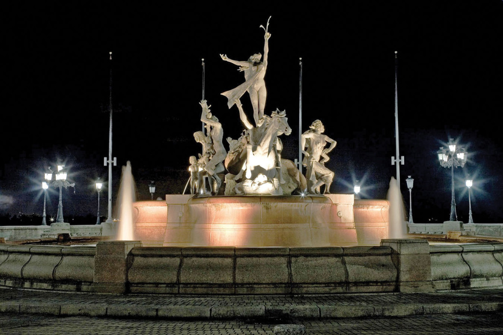 A fountain with sculpted figures lit up at night.