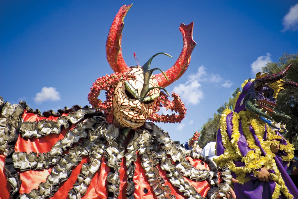 An elaborate carnival costume with a horned mask and wide ruffled collar in reds and golds.