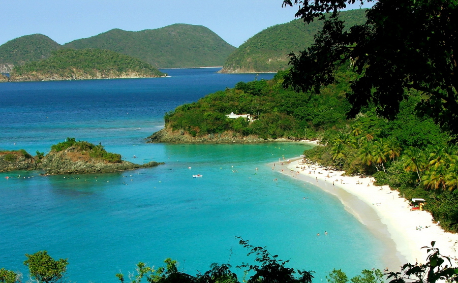 View down into Trunk Bay with a strip of white sandy beach and a tiny island jutting up out of the water.