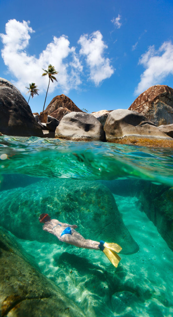 A woman snorkels amid boulders under Virgin Gorda's blue skies.