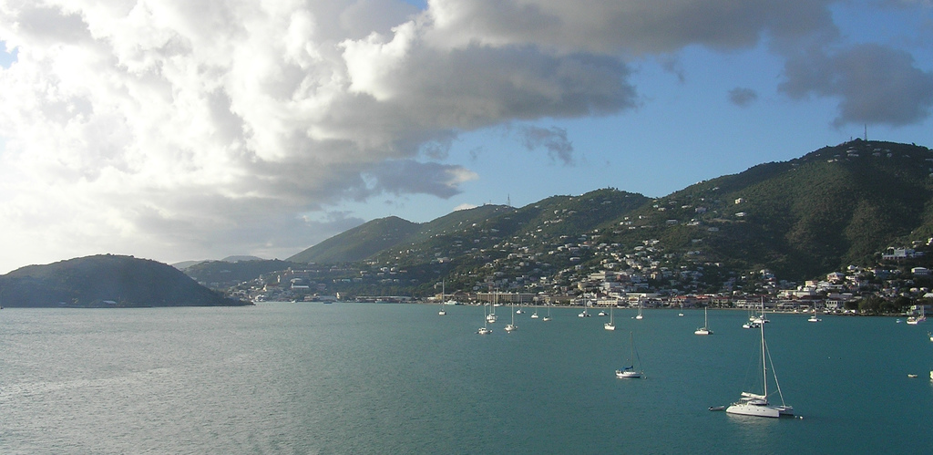 Sailboats dot the water of the bay as the verdant hills of the island rise up in the distance.