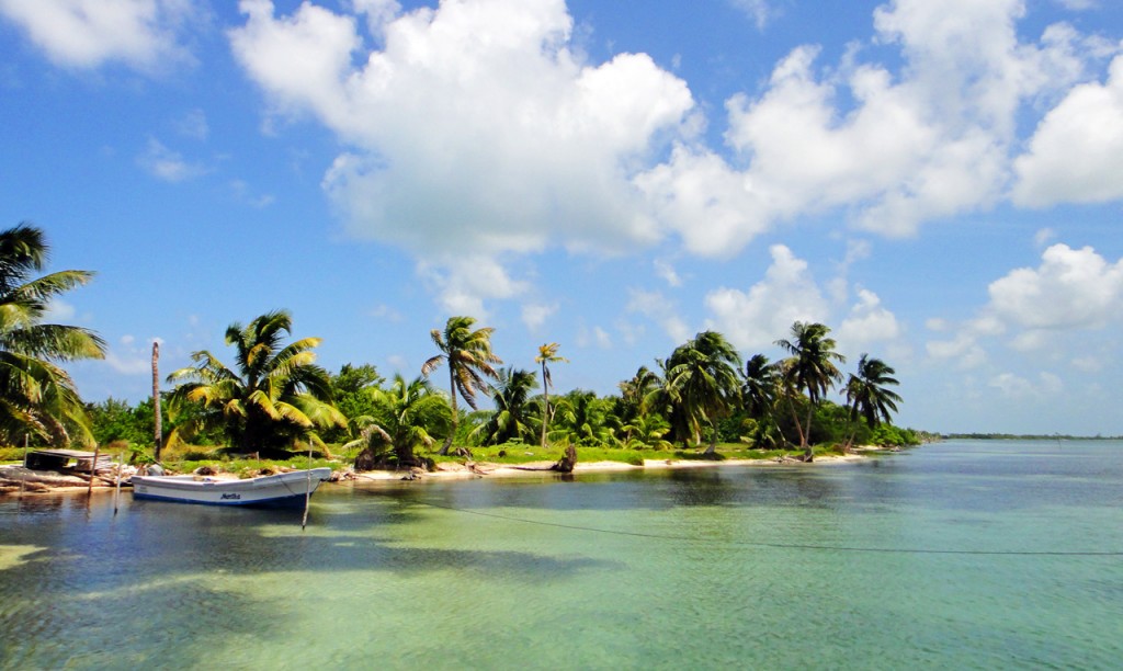 A boat is docked along a strip of shore surrounded by calm, clear water.