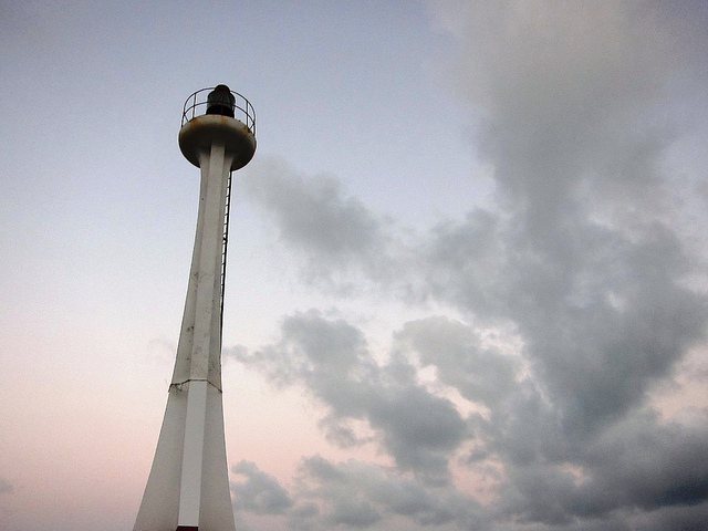 Looking up at the top of narrow Fort George Lighthouse silhouetted against the sky.