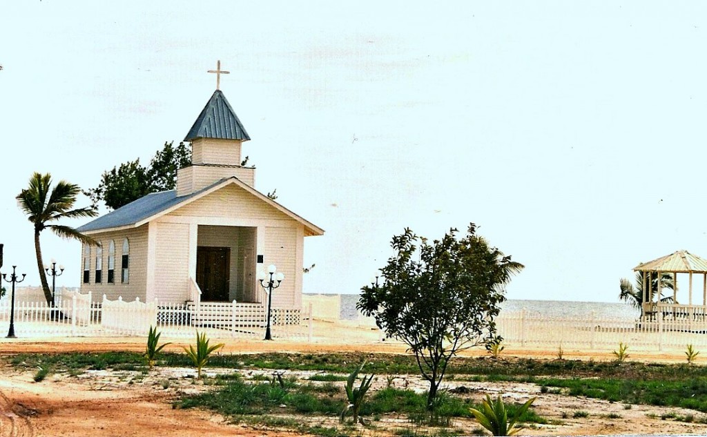 A simple one-room church with a picket fence near the shore.