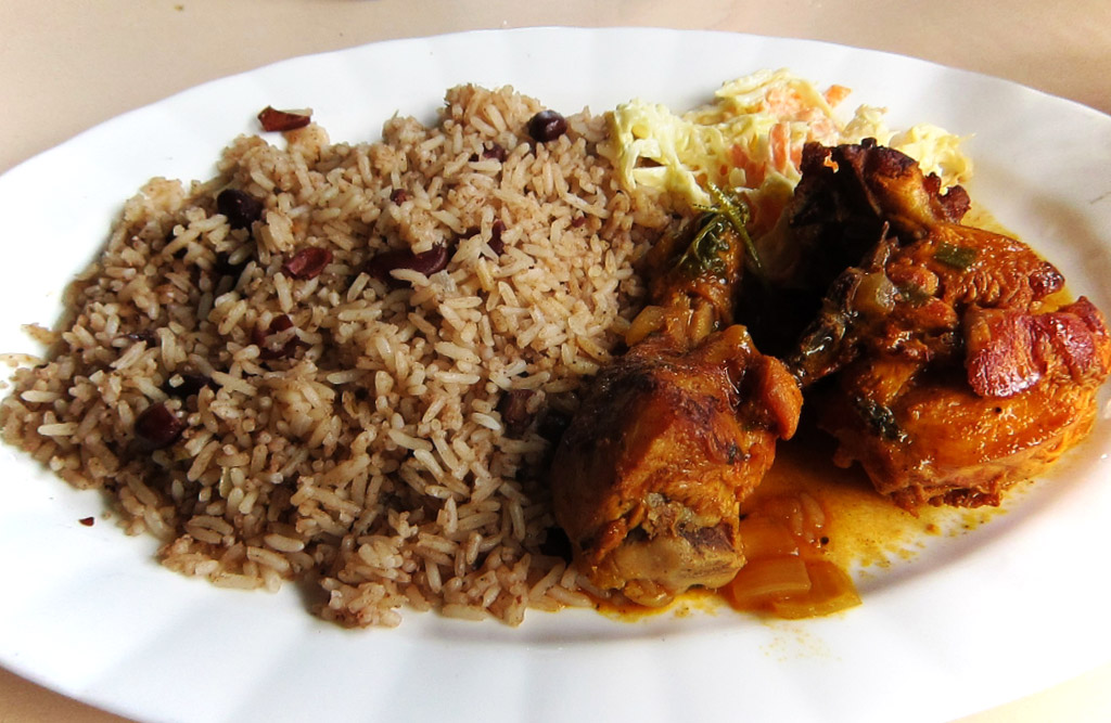 A plate heaped with rice and a couple pieces of chicken stewed with a reddish-orange tint.