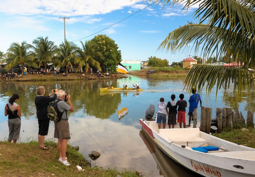 Viewers on shore watch as three men paddle a canoe in.