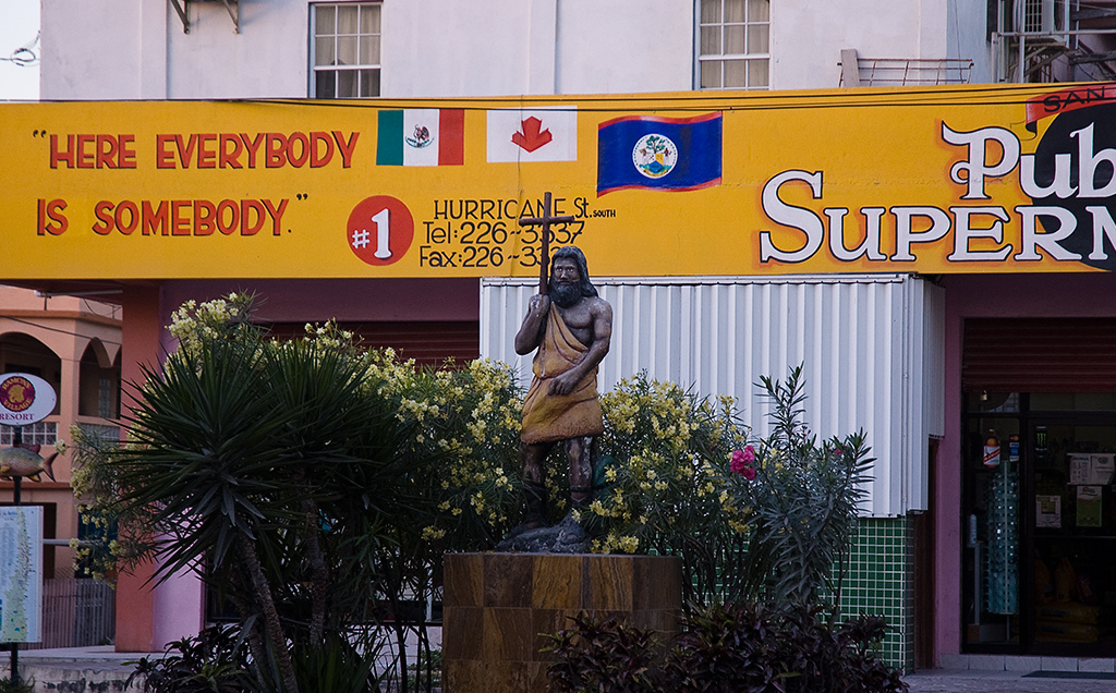 A sculpture of Jesus holding a cross stands in front of a market banner reading Here Everybody is Somebody.